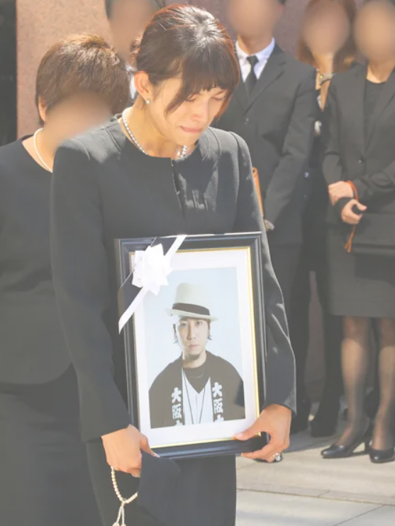上原多香子が夫の葬式に出席して夫の写真をもって立っている姿